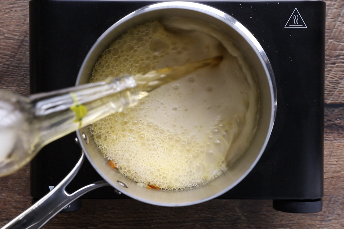 Pouring a glass of beer in a pan with carrots and onions