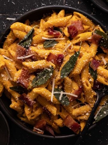 Pumpkin pasta with bacon, sage, and parmesan cheese on a black plate