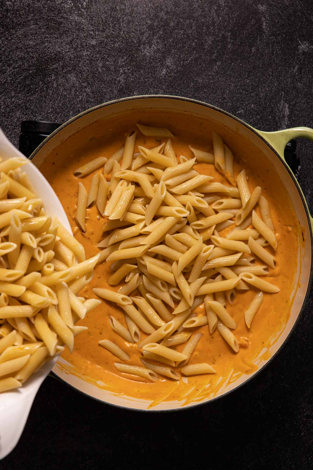 Penne pasta pouring into a saute pan with creamy pumpkin sauce