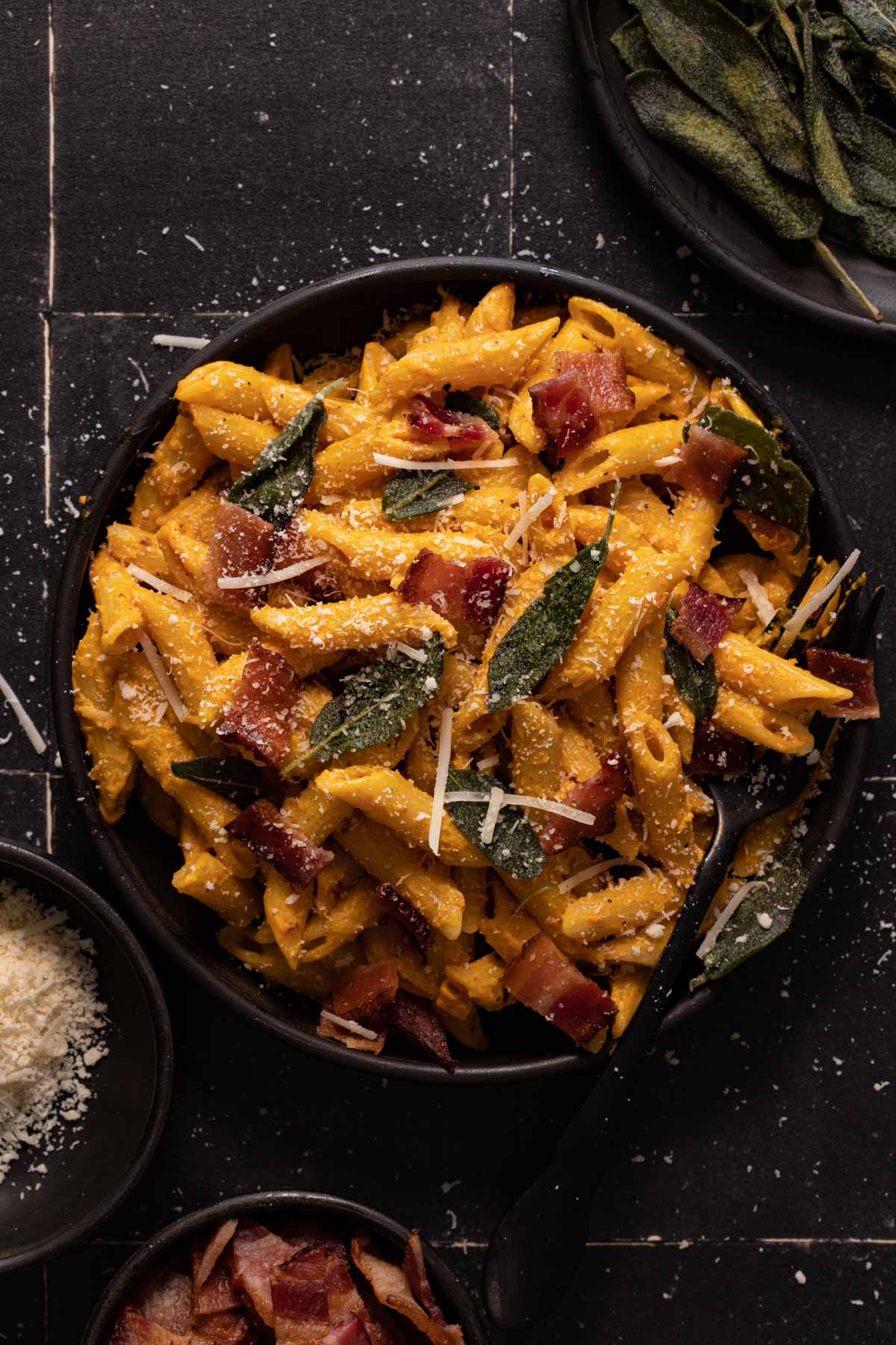 Creamy pumpkin pasta with bacon and sage on a black plate