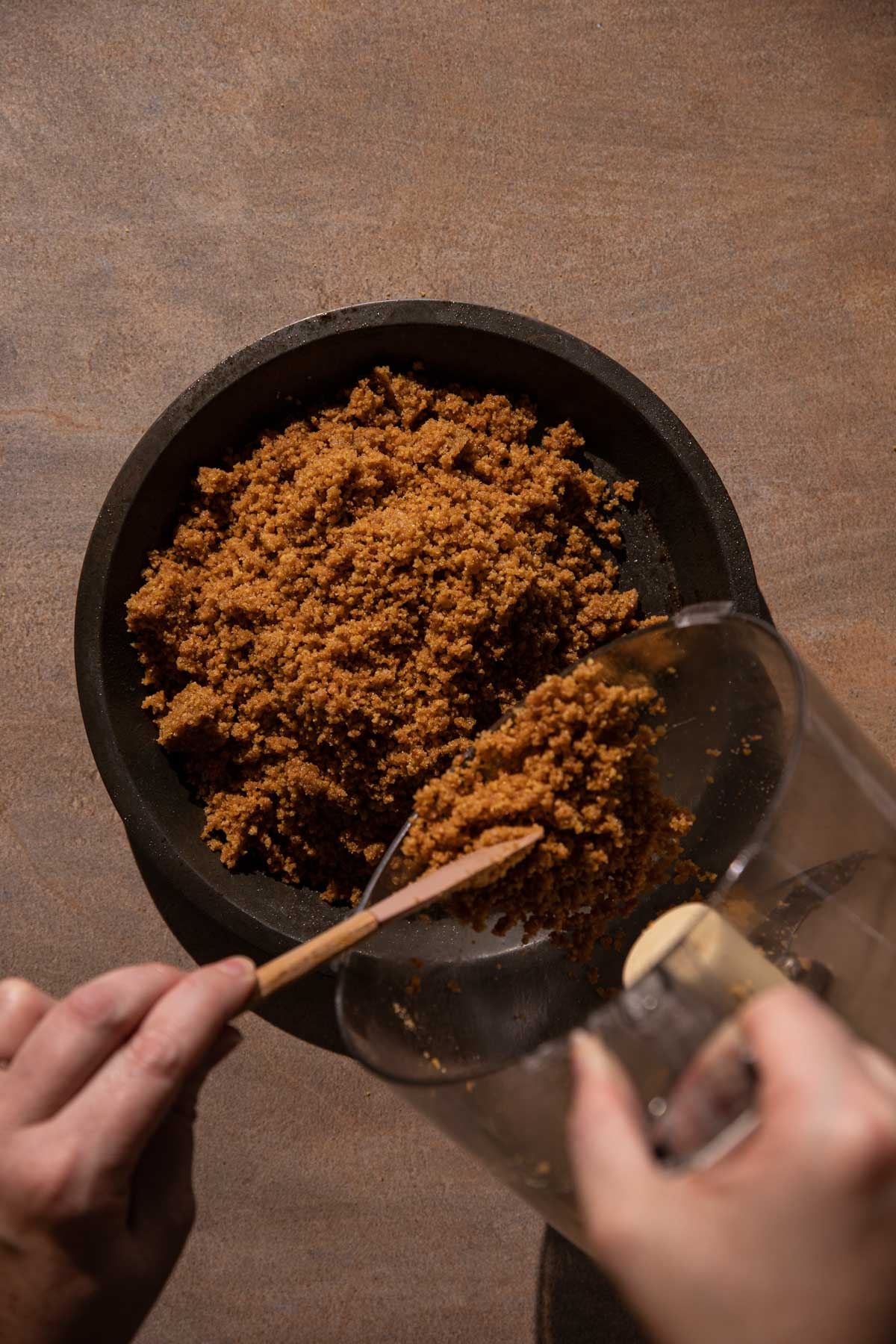 Hands pouring gingersnap crust in a pie pan