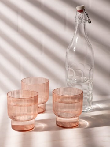 Three pink glasses in light with window blind shadows