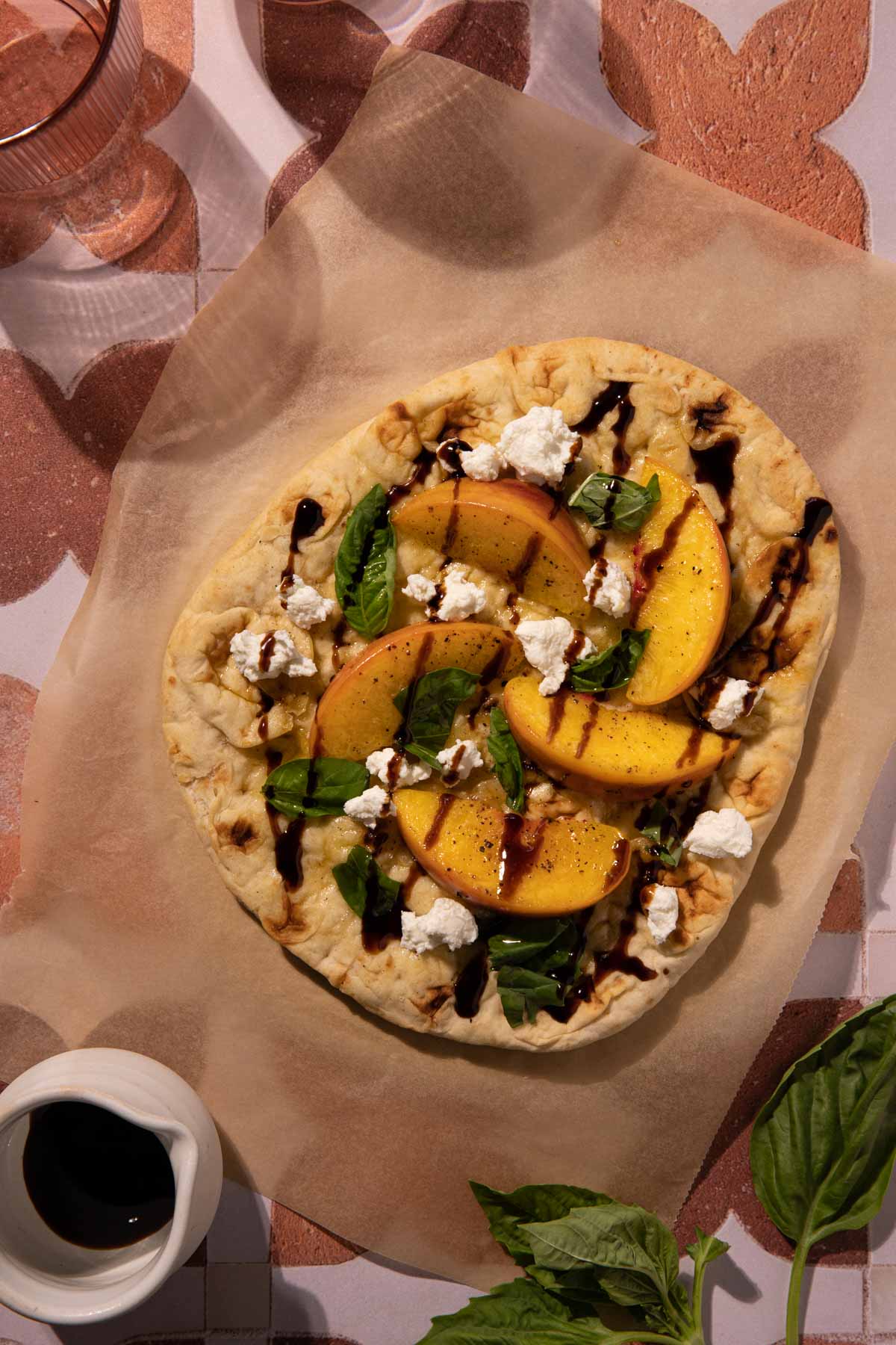Grilled peach flatbread on parchment paper with a bowl of balsamic vinegar