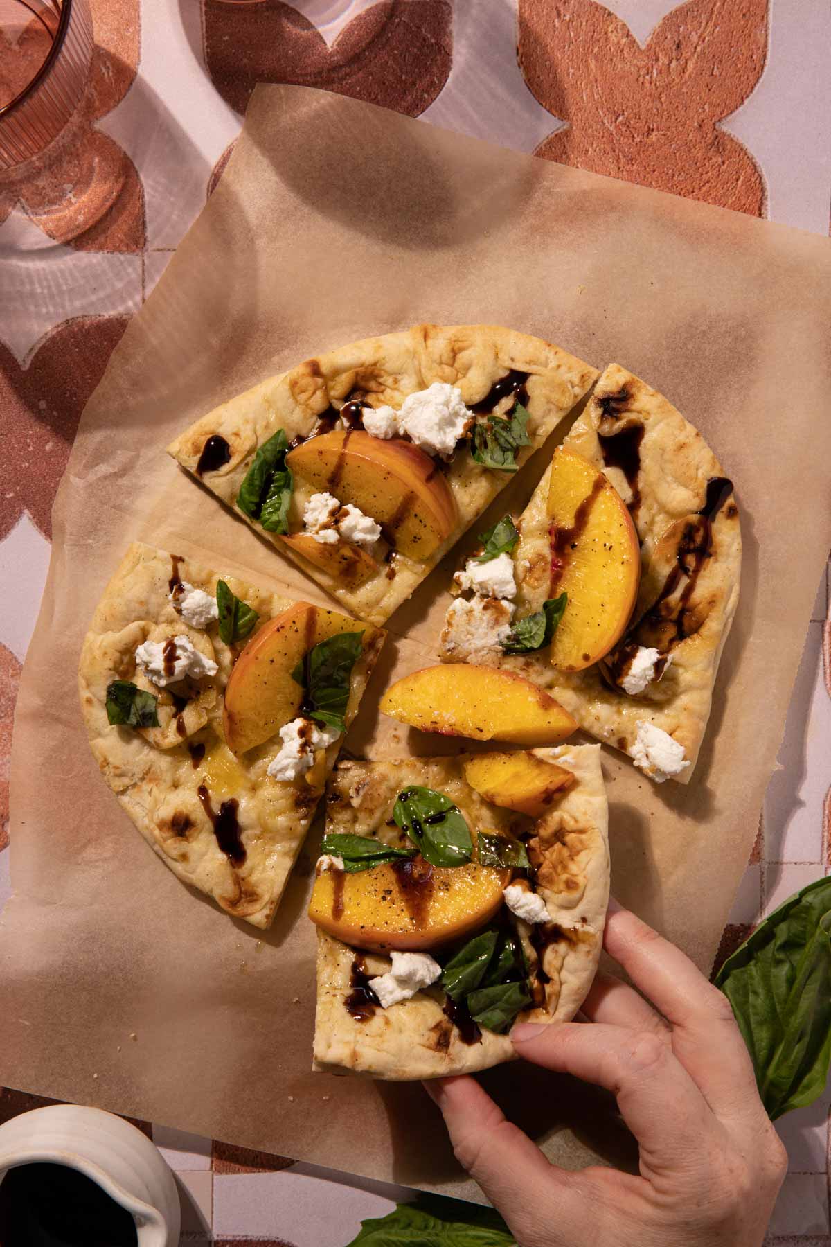 A hand holding a slice of grilled peach flatbread