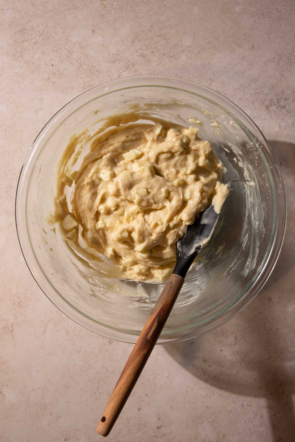 Apples in cake batter in a bowl with a spatula