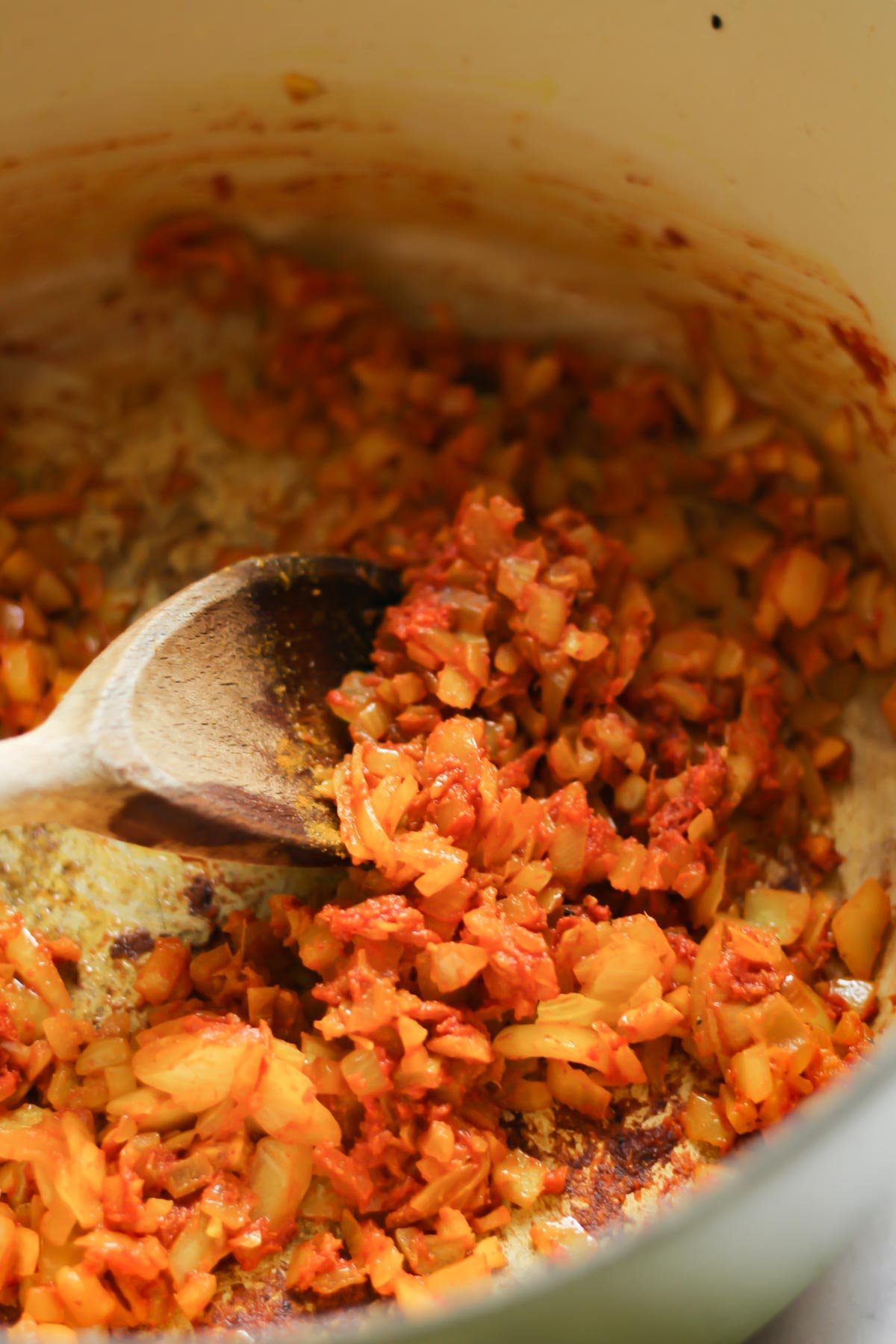 Onions, red curry paste, and turmeric sauteeing in a pot with a wooden spoon