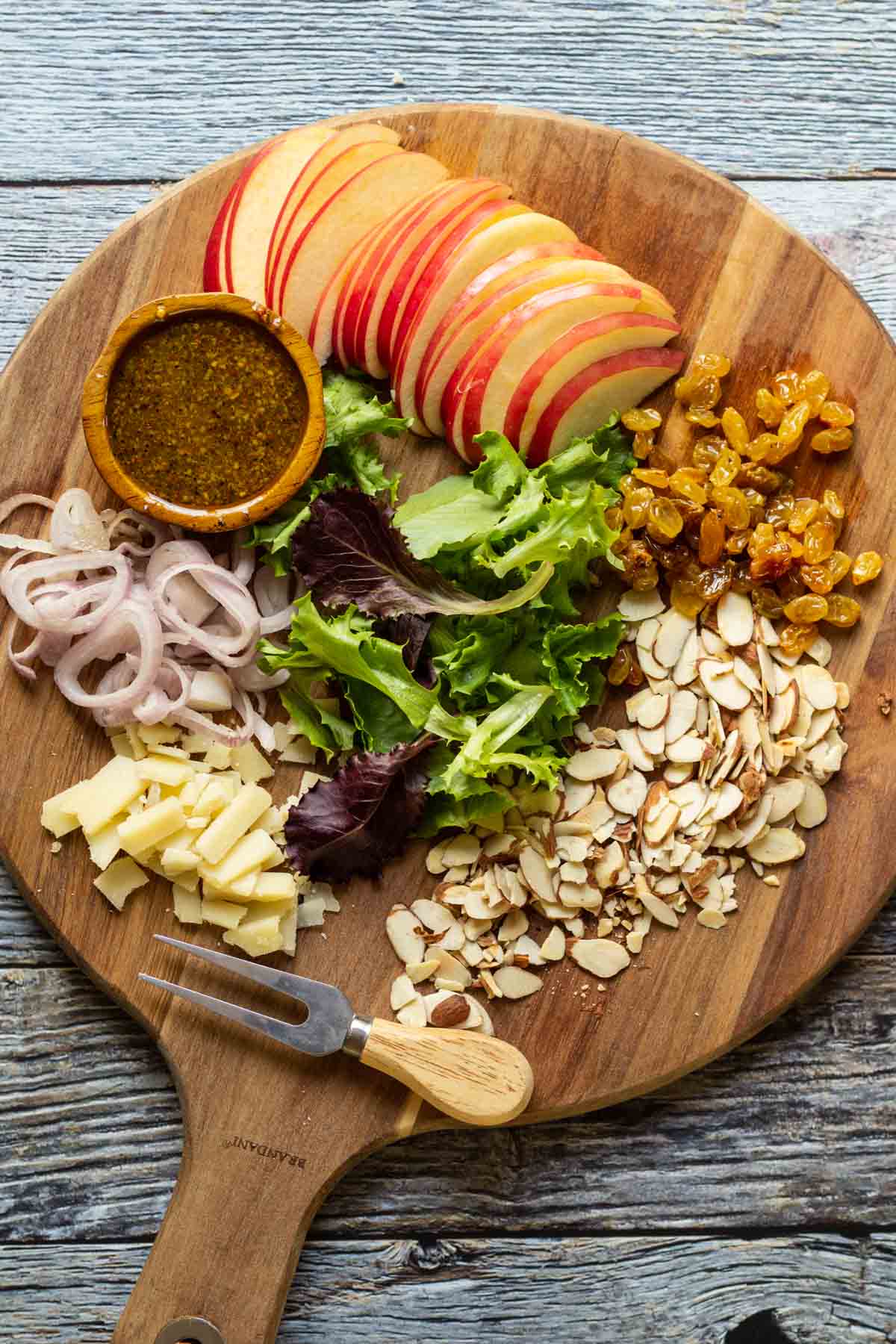 Sliced apples, mixed green salad, nuts, and cheese on a wooden board