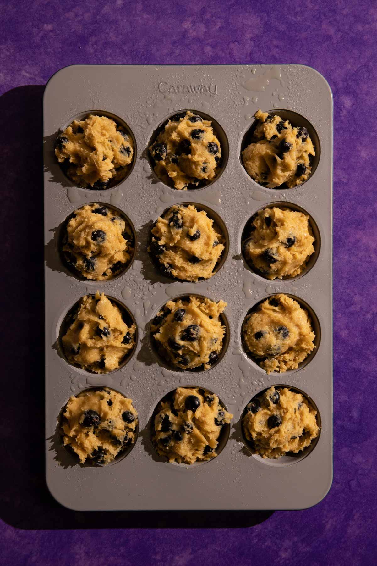 12 scoops of blueberry muffin batter in a muffin pan 