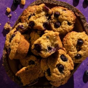 A blueberry with a bite taken out of it on top of muffins in a basket