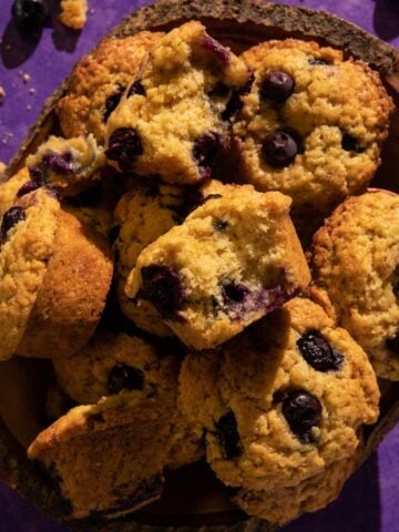 A blueberry with a bite taken out of it on top of muffins in a basket