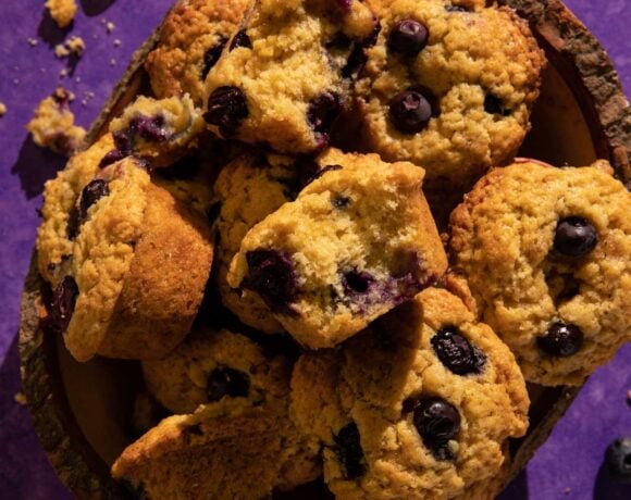 A blueberry with a bite taken out of it on top of muffins in a basket