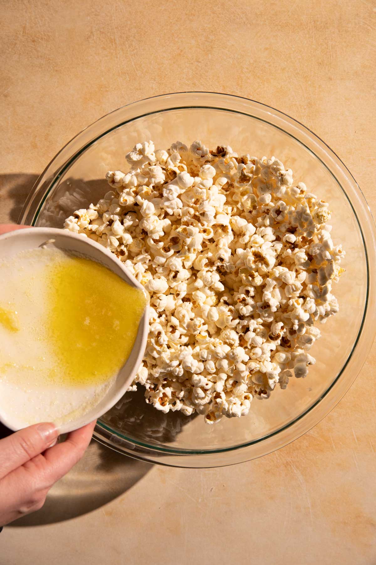 Pouring melted garlic butter on top of the popcorn in a bowl