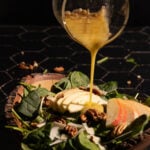 Apple cider vineger dressing being poured over an apple salad in a bowl