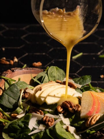 Apple cider vineger dressing being poured over an apple salad in a bowl