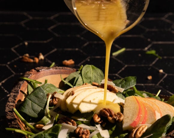Apple cider vineger dressing being poured over an apple salad in a bowl