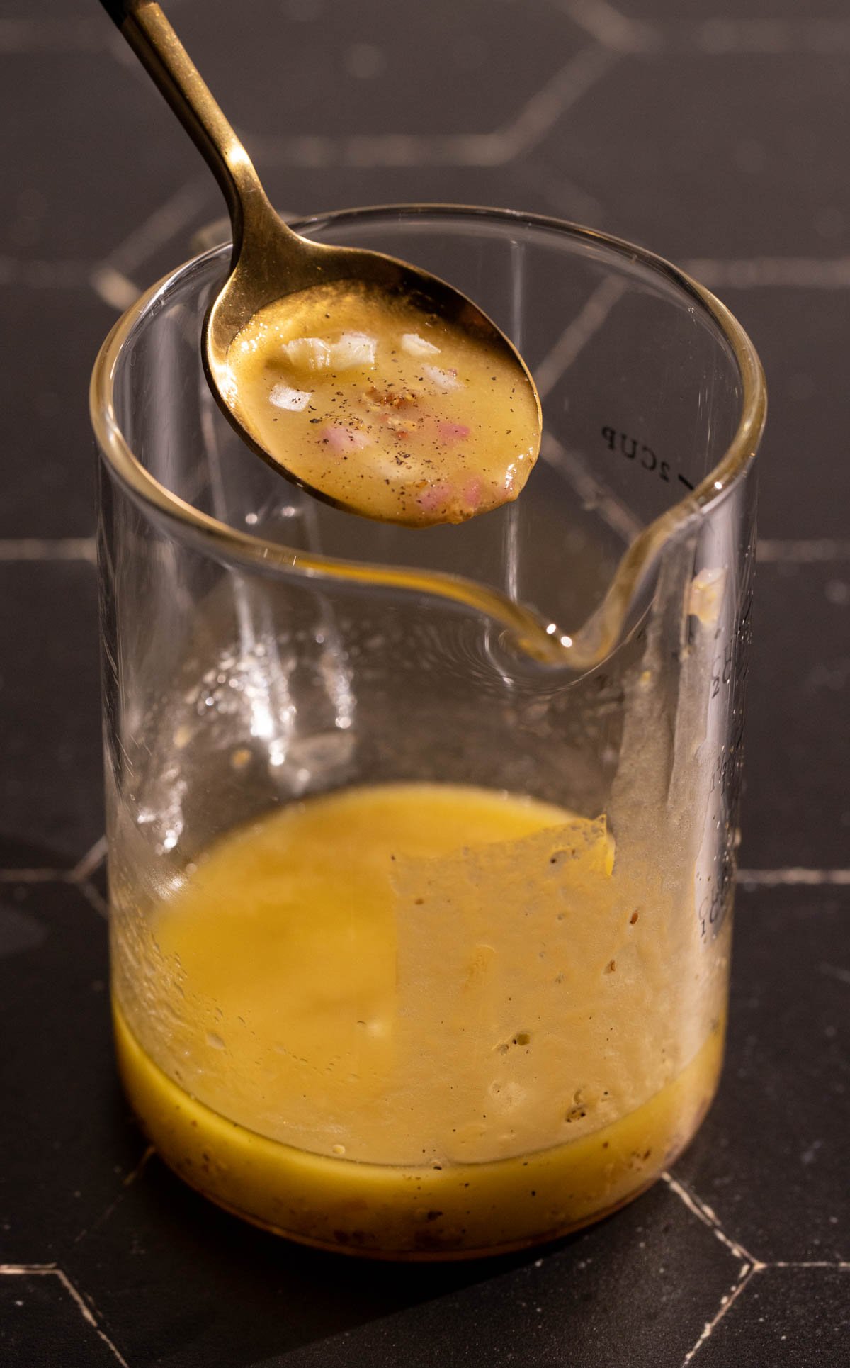 A spoon over a glass cup of apple cider vinegar dressing