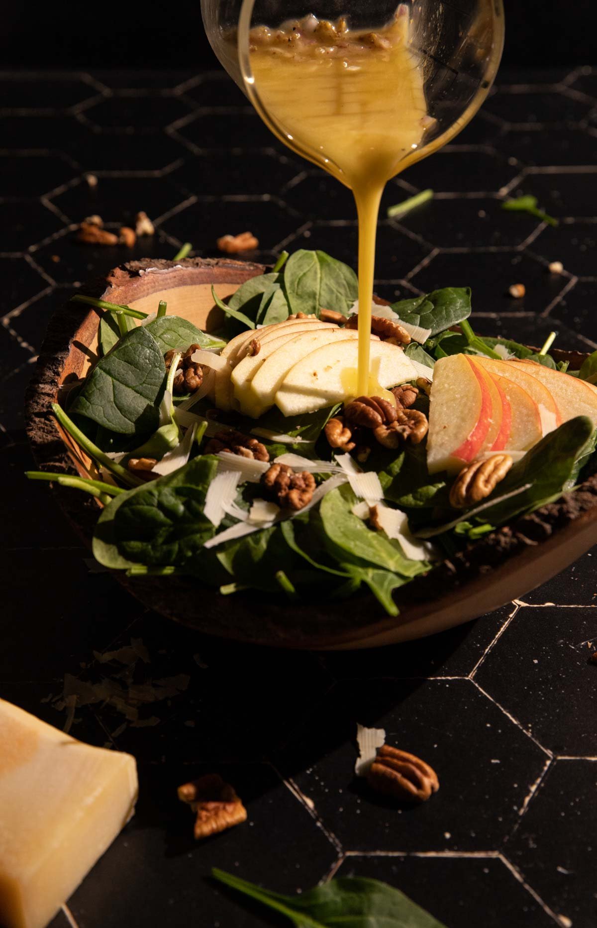 A glass pouring apple cider vinegar dressing over a salad in a bowl