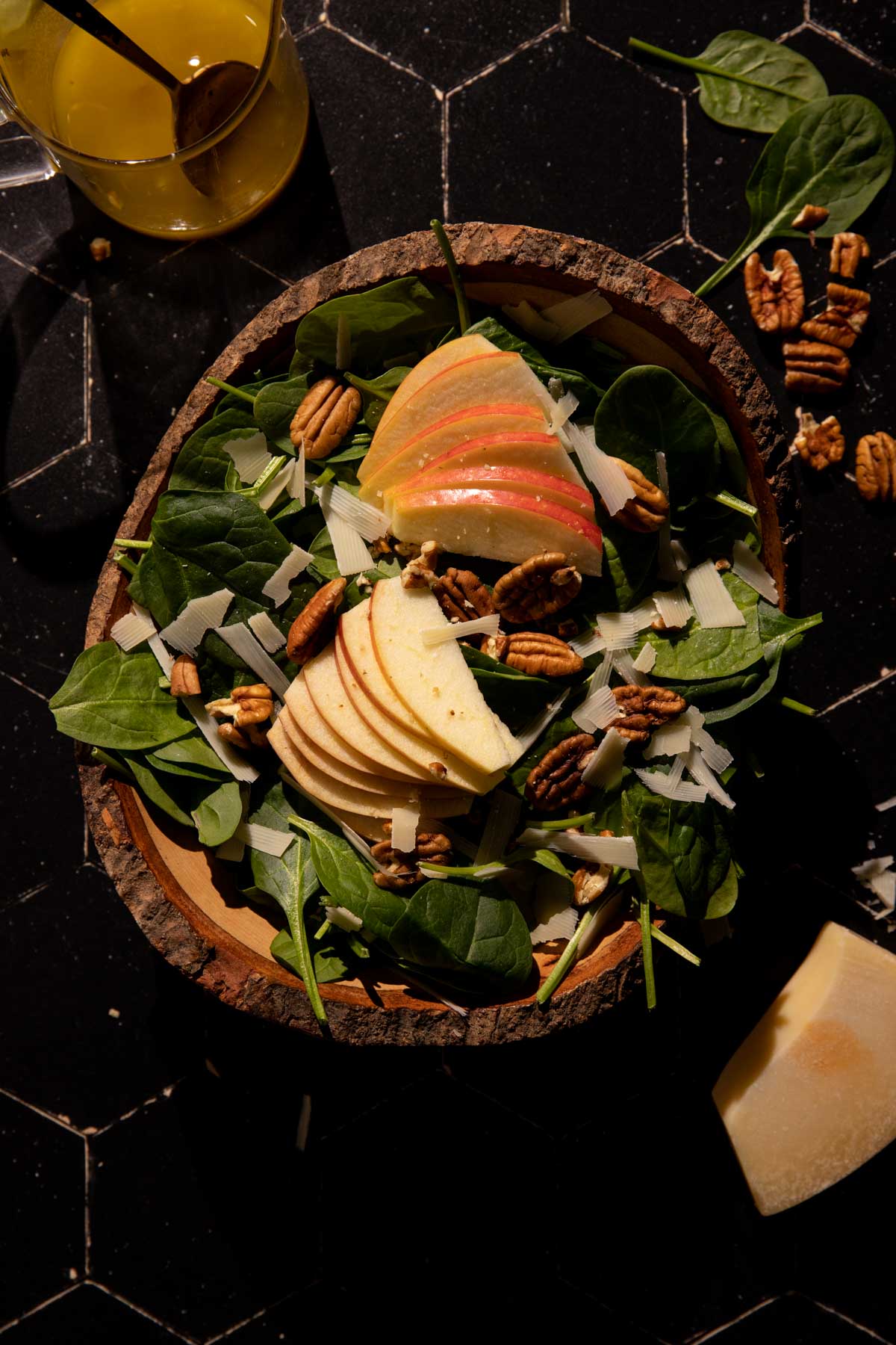 A spinach apple salad in a bowl with parmesan and pecans