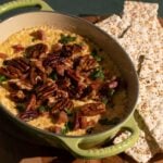 A baking dish of herbed goat cheese served with crackers and garnished with pecans and bacon.