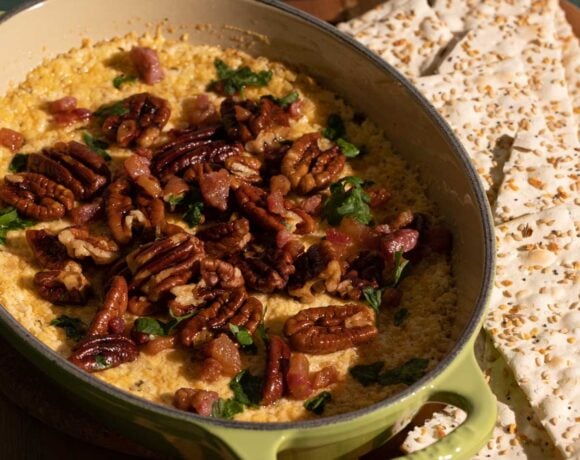 An oven dish with baked goat cheese dip, garnished with toasted pecans.