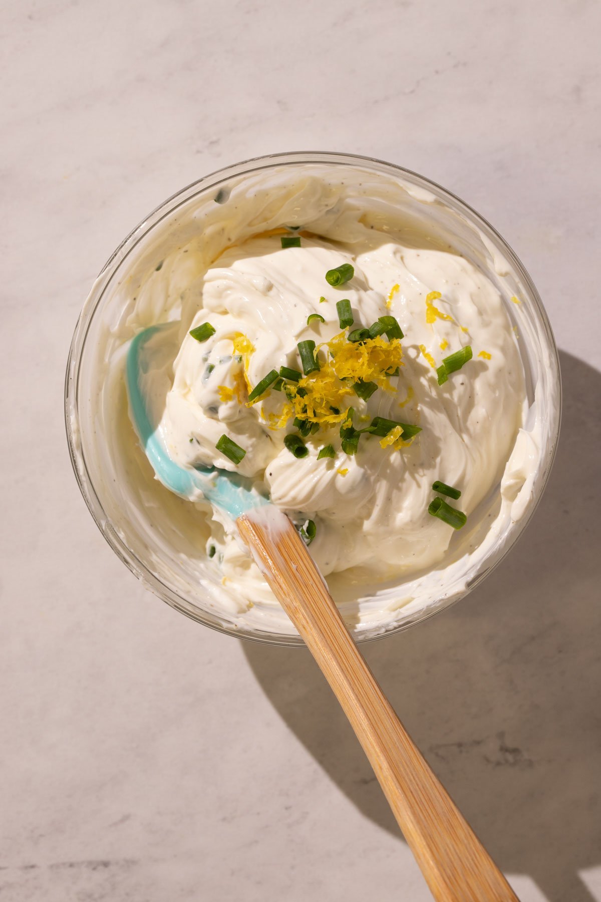 A small bowl of cream cheese spread with fresh chives and lemon zest on top.
