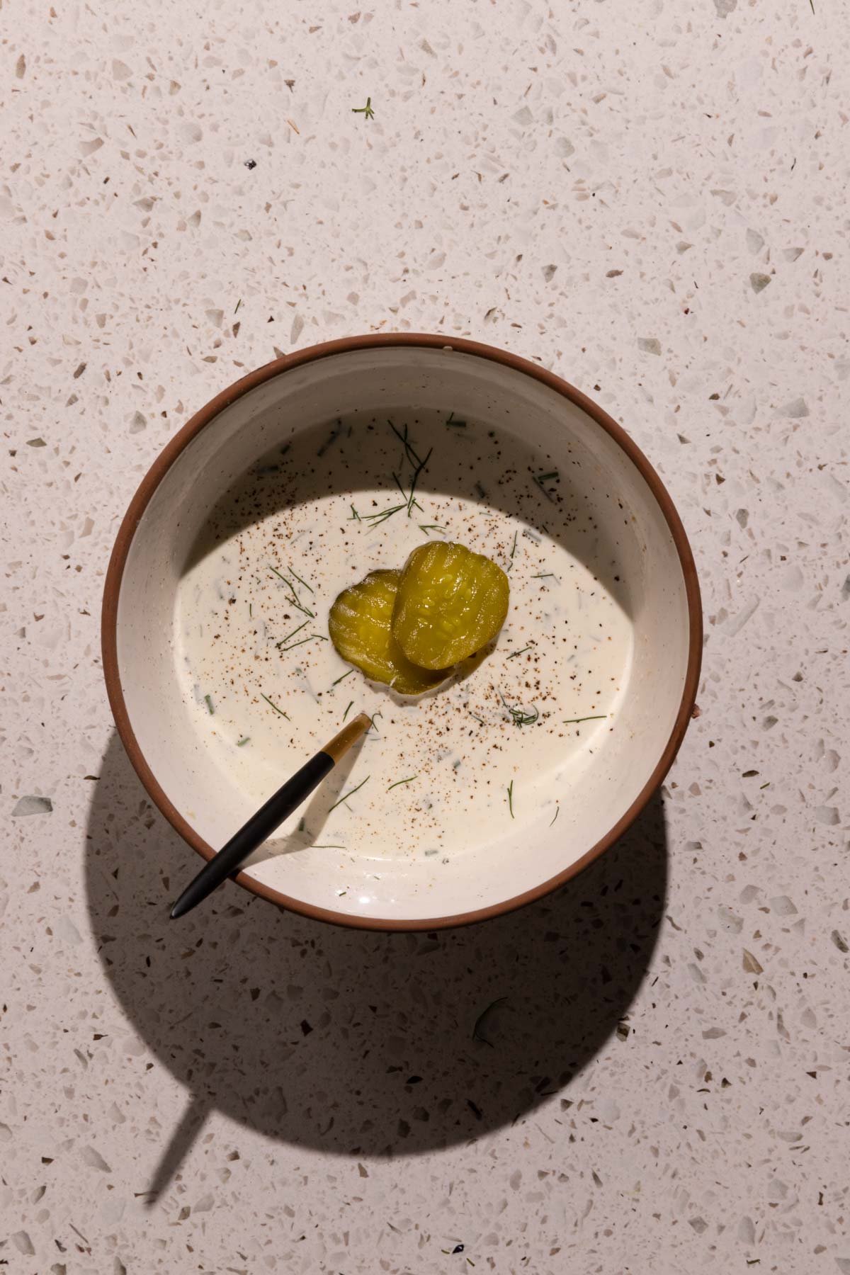 A bowl of dill pickle ranch dressing with pickles on top