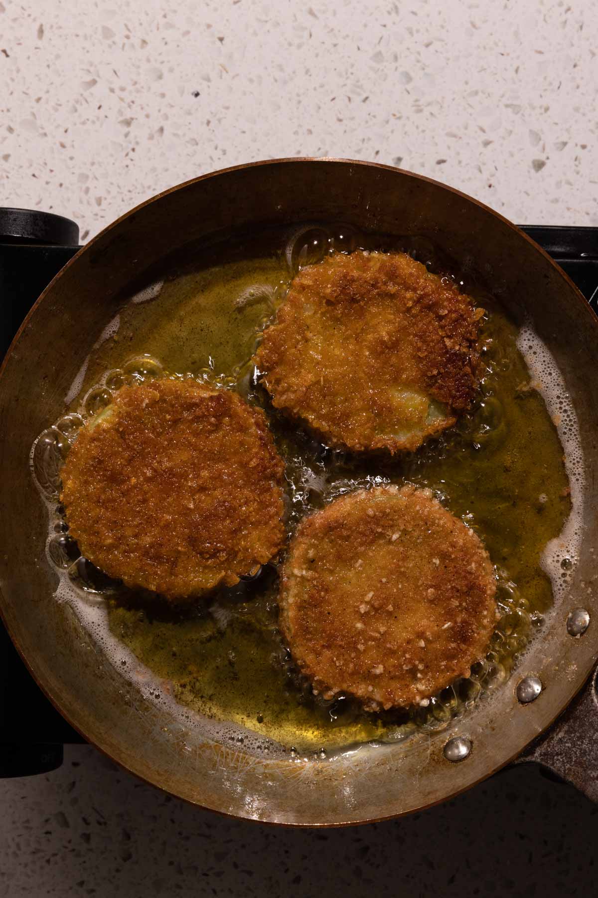 Fried Green Tomatoes frying in a pan with oil