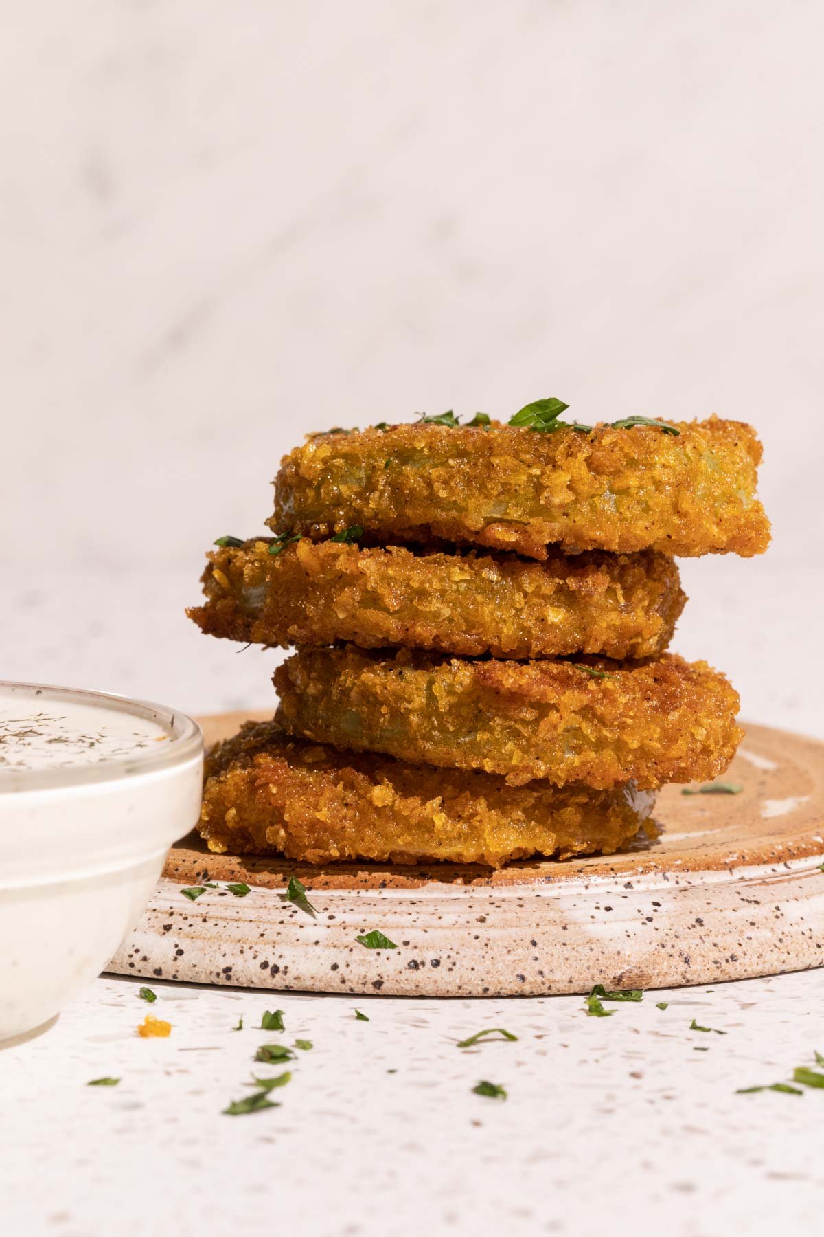 Fried green tomatoes stacked on a plate with dill pickle ranch dip in a bowl