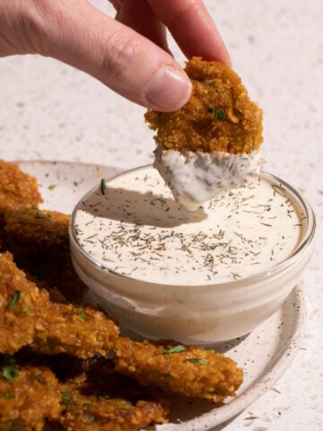 A hand with a fried pickle dipping in dill pickle ranch dressing