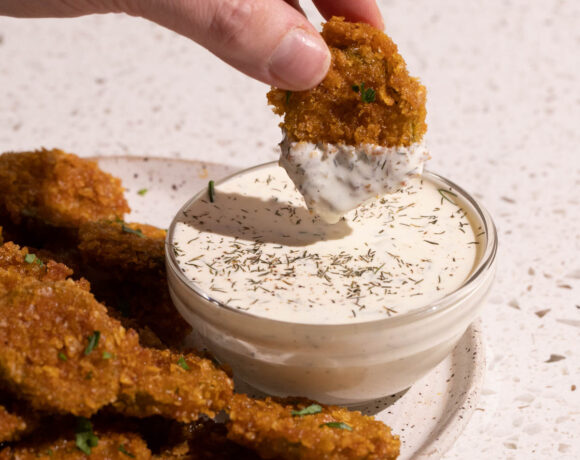 A hand with a fried pickle dipping in dill pickle ranch dressing