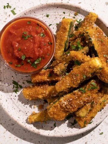 Fried zucchini sticks on a plate with marinara sauce