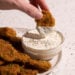 A hand with a fried pickle dipping in dill pickle ranch dressing